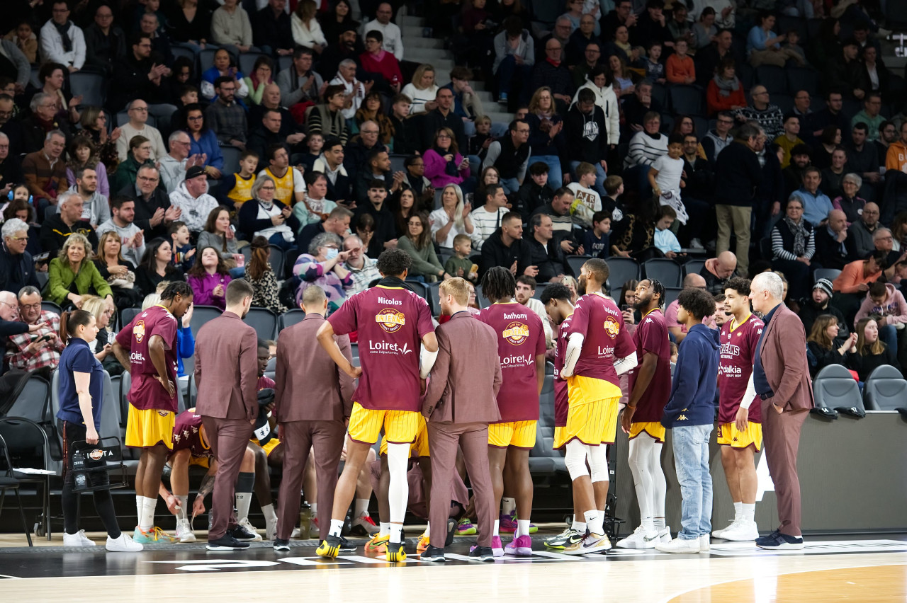 A team huddle on the court during a timeout, with the arena crowd behind them