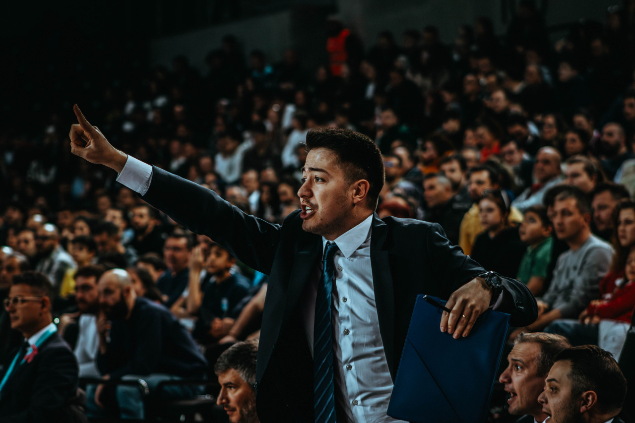 A basketball coach directing from the sideline during a packed indoor game